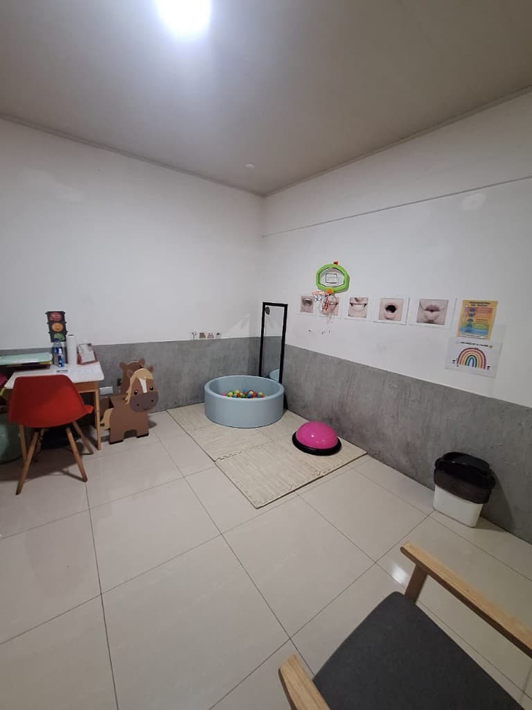 Sala de terapia infantil con espacio de juego, espejo y materiales para estimulación del lenguaje.